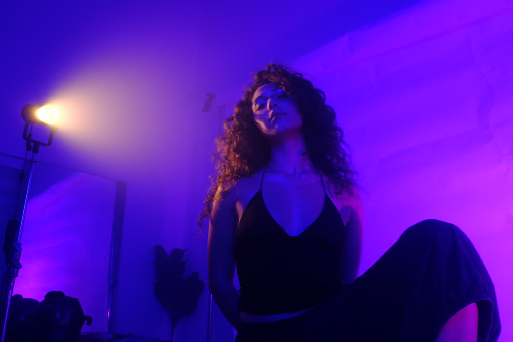 Bella Valdes on a violet-lit stage, head tilted back, a warm lamp flaring behind her.